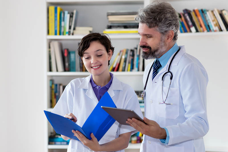 Die Praxis als Lernort Arzt und Krankenschwester sprechen über Patient, die Krankenschwester hält eine Akte in der Hand, der Arzt einen Tablet-PC